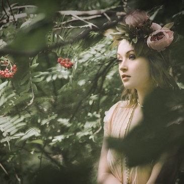 Natural light portrait of a young woman wearing a flower crown framed by leaves in a wooded area