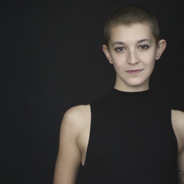 Natural light portrait of a young woman with a shaved head and tattoos looking at the camera
