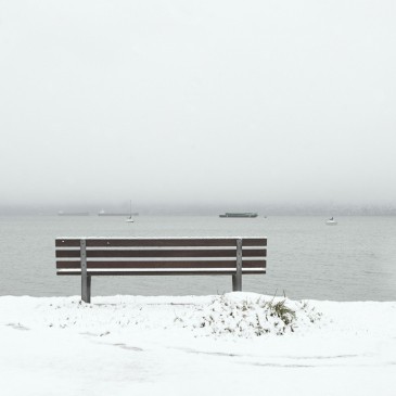 Park bench overlooking the water at Kitsilano Yacht Club looking towards West Vancouver on a snowy day in Vancouver BC