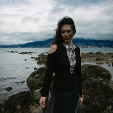Outdoor natural light portrait of a woman on a rocky shoreline with moody cloudy skies and the wind blowing her curls into her face