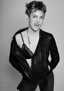 Black and white portrait of a young woman wearing a black bralette, jeans and leather biker jacket pulling a face for the camera
