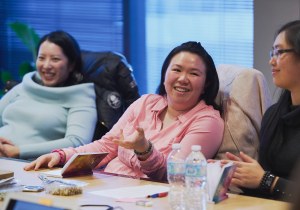 Image of a woman gesturing and laughing as other women around her listen and smile during a self care workshop in Vancouver